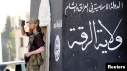 FILE - A militant Islamist fighter uses a mobile to film his fellow fighters taking part in a military parade along the streets of Syria's northern Raqqa province.