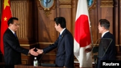 Perdana Menteri China Li Keqiang (kiri) berjabat tangan dengan Perdana Menteri Jepang Shinzo Abe (tengah), disaksikan oleh Presiden Korea Selatan Moon Jae-in dalam konferensi pers kerja sama trilateral Jepang-China-Korea Selatan di Tokyo, 9 Mei 2018.
