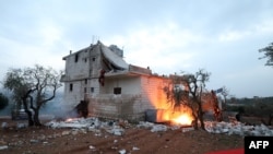 FILE - Red tape is extended and objects are set on fire, around the house in which the leader of Islamic State (IS) group Amir Mohammed Said Abd al-Rahman al-Mawla died, during an overnight raid by US special forces.
