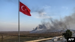 Asap membubung dari Tal Abyad, sebuah kota di Suriah. Foto diambil dari perbatasan Turki di mana tampak bendera Turki di Akcakale, 10 Oktober 2019. 