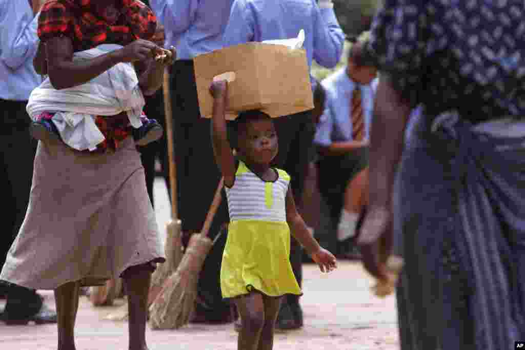 Seorang anak perempuan berjalan sambil membawa barang di atas kepalanya di kota Harare, Zimbabwe.