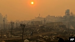 A couple walks through a neighborhood destroyed by wildfires in Chile's Santa Olga community, Jan. 26, 2017. Officials say the town was consumed by the country's worst wildfires.