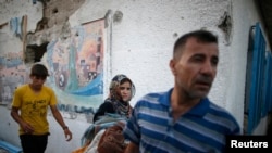 Seorang perempuan membawa barang-barangnya di sebuah sekolah yang dikelola PBB yang menampung warga Palestina, terkena gempuran tank Israel.