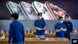 FILE - Employees wear face masks as they stand in a reopened Apple Store in Beijing, Feb. 14, 2020. 