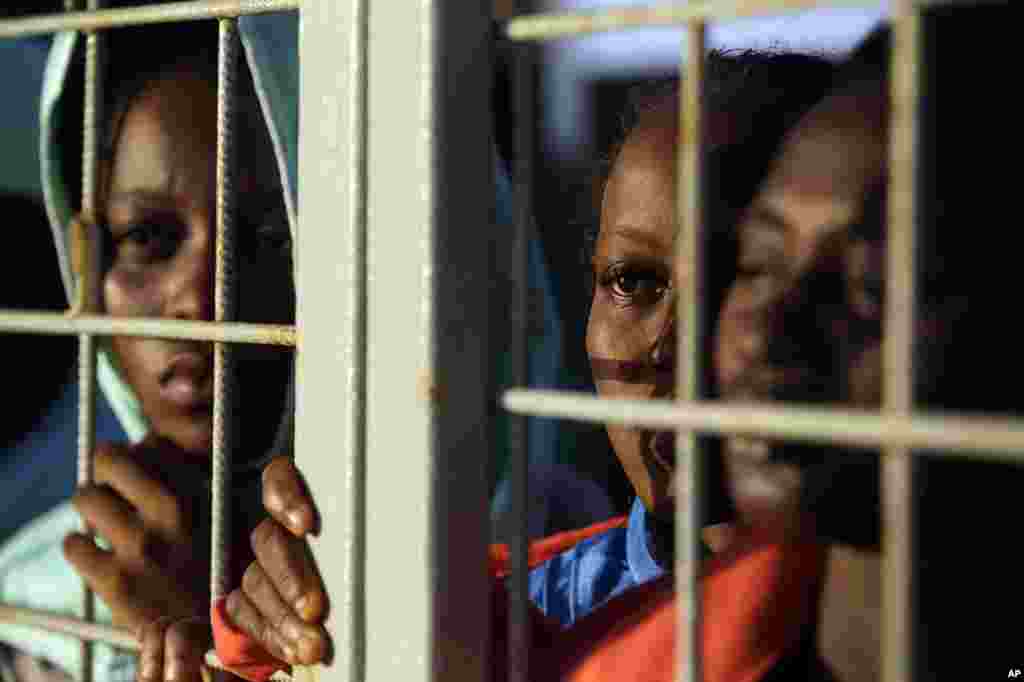 Migrants rescued off the Libyan coast peer out of a gate on the Siem Pilot Norwegian ship to get the first sight of Sardinia island as they sail in the Mediterranean sea toward the Italian port of Cagliari, Sept. 3, 2015.