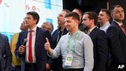 Ukrainian President Volodymyr Zelenskiy, center, reacts with his team as they look at the election results at his party's headquarters after a parliamentary election in Kiev, Ukraine, Sunday, July 21, 2019.