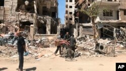 People stand in front of damaged buildings, in the town of Douma, the site of a suspected chemical weapons attack, near Damascus, Syria, April 16, 2018.
