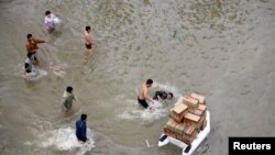 在被大水淹没的余姚街道上，一名用充气阀运送食品的志愿者被一名男子推倒在水中，别人在一旁观望。（资料照）