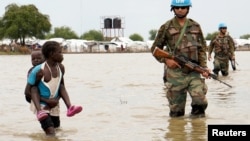 Une fillette tenant un bébé passe devant des soldats de la paix de l'ONU, après que de fortes pluies et des inondations ont forcé des centaines de milliers de personnes à quitter leurs maisons, dans la ville de Pibor, dans l'État de Boma, au Soudan du Sud, le 6 novembre 2019.