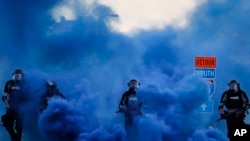 Police in riot gear walk through a cloud of blue smoke as they advance on protesters near the Minneapolis 5th Precinct, May 30, 2020, in Minneapolis. 