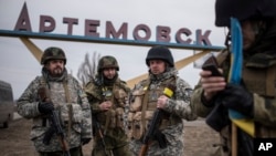 FILE - Ukrainian servicemen stand at the sign reading Artemivsk, eastern Ukraine, March 3, 2015. Some European Union member states want to give the fragile cease-fire with Russia more time. 