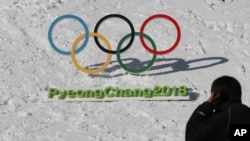 In this Friday, Feb. 3, 2017 photo, a man walks by the Olympic rings with a sign of 2018 Pyeongchang Winter Games.