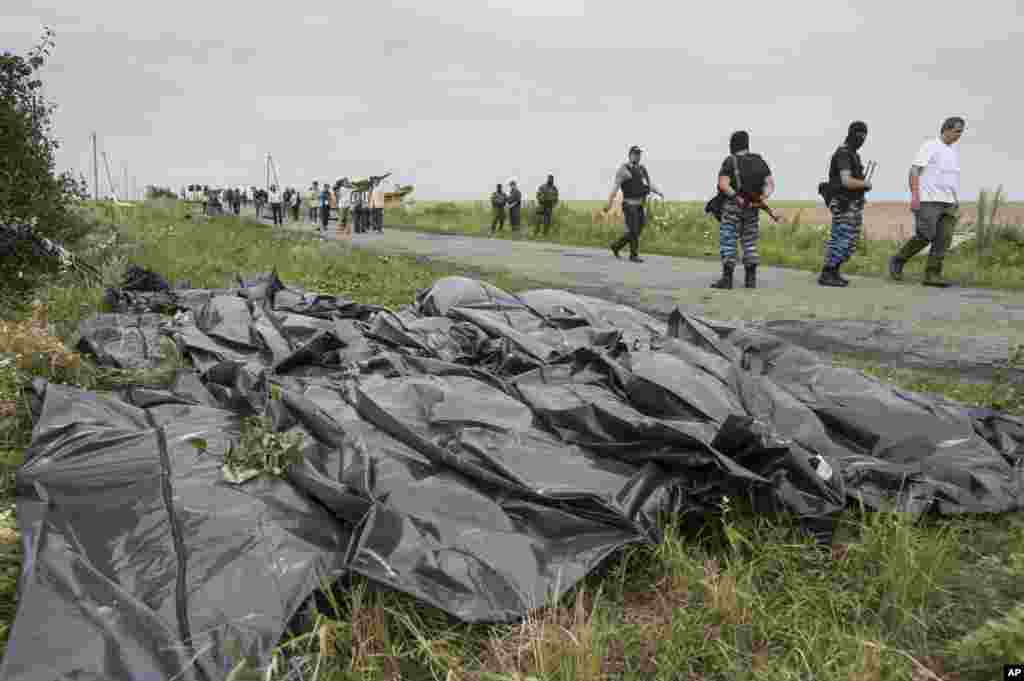 Para pemberontak pro-Rusia berjalan di jalan tempat jenazah-jenazah korban dibaringkan dalam kantong di dekat jatuhnya pesawat Malaysia Airlines dekat desa Hrabove, Ukraina timur (19/7).&nbsp;(AP/Evgeniy Maloletka)