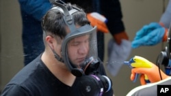 A Servpro cleaning worker has his respirator mask sprayed down Thursday, March 12, 2020, as he gets ready for a break from his work cleaning inside the Life Care Center in Kirkland, Wash., near Seattle. (AP Photo/Ted S. Warren)