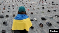 Seorang perempuan menatap ratusan sepatu yang melambangkan kejahatan perang yang dilakukan terhadap warga sipil Ukraina di Alun-alun Kota Tua untuk memperingati satu tahun invasi Rusia ke Ukraina, di Praha, Republik Ceko, 15 Februari 2023. (Foto: REUTERS/David W Cerny)