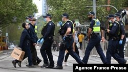 People carry their shopping as police patrol in Melbourne, Australia, Sept. 30, 2021, as the city grapples with a surge in COVID-19 infections.