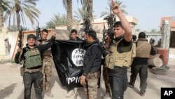 FILE - Iraqi security forces celebrate as they hold a flag of the Islamic State group they captured in Ramadi, 70 miles (115 kilometers) west of Baghdad, Iraq. 